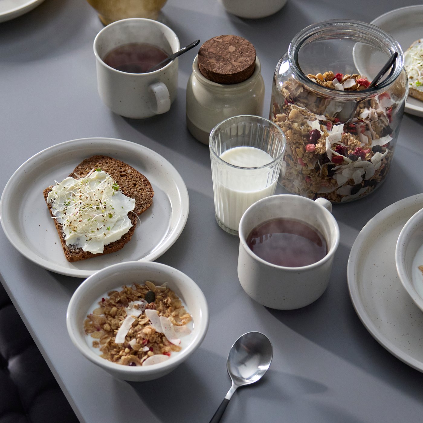 A grey table displays a DAGGASTER plate with two slices of rye toast and a DAGGASTER bowl with granola and milk.