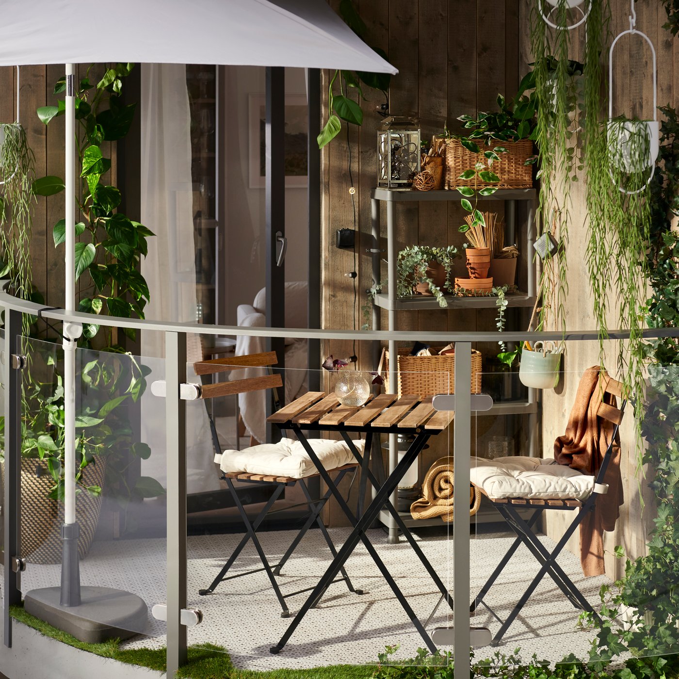 Un piccolo balcone con molti elementi in legno, piante appese, un tavolo TÄRNÖ, sedie TÄRNÖ e uno scaffale RUNMARÖ.