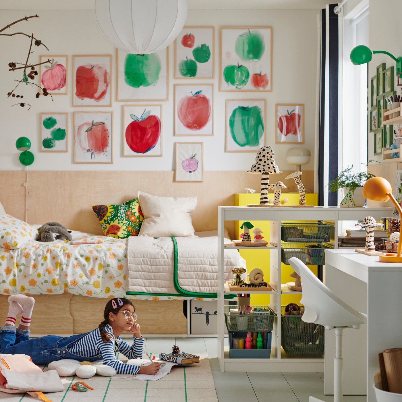 A young girl lies reading on a rug in front of a KLIPPUGGLA bed frame with storage, dressed in floral bedding and pillows.