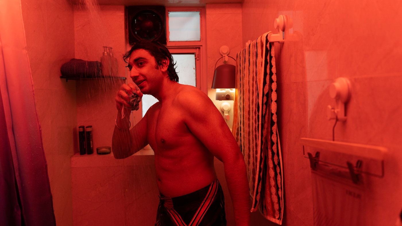Man standing in the shower in a bathroom lit with red lighting, singing along to music coming from a VAPPEBY Bluetooth speaker.