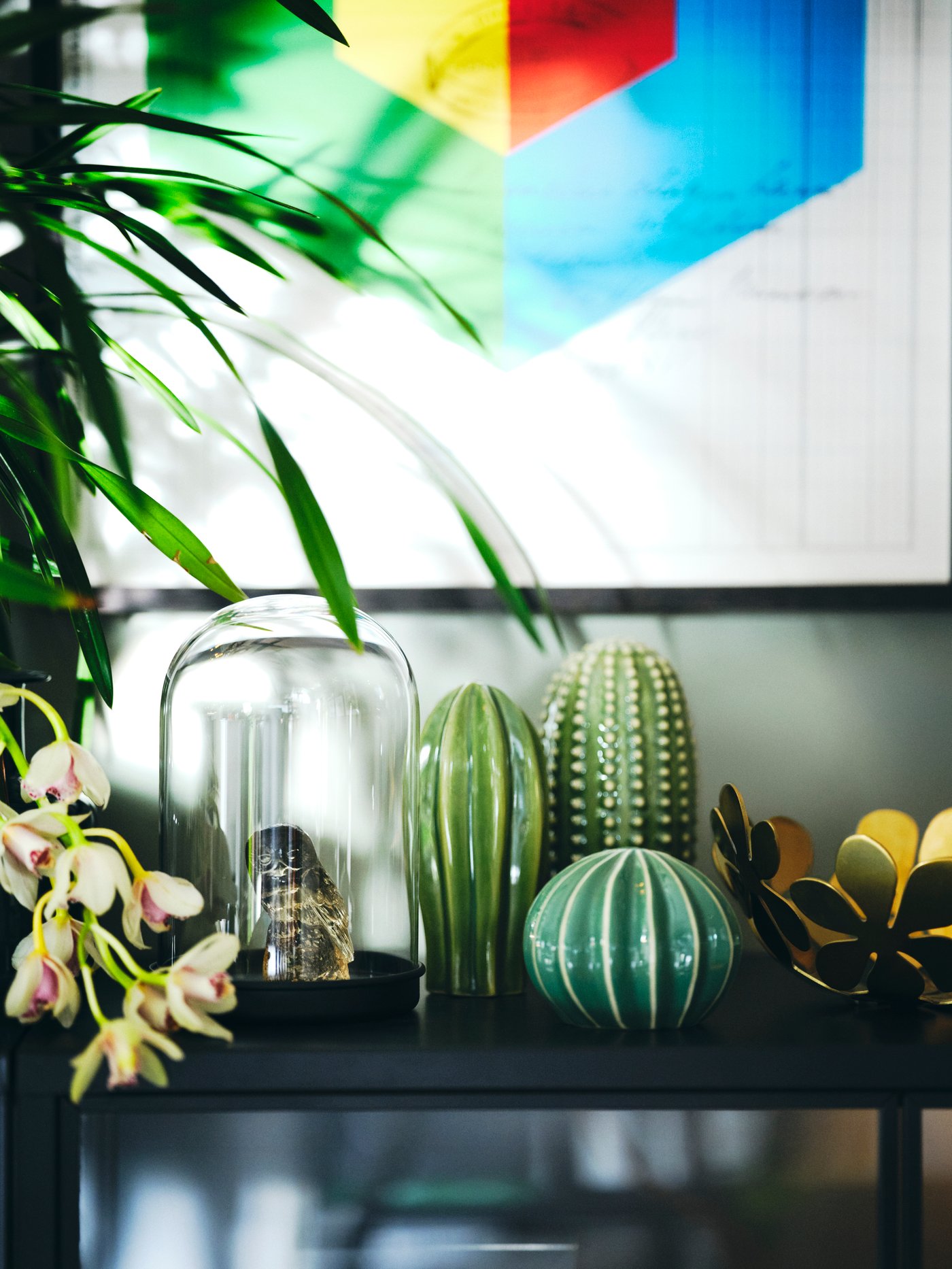 Grønne keramikfigurer ved siden af en guld metal skål på en skænk med et grafisk billede over.