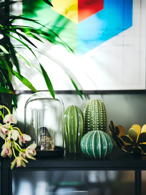 A glass dome with black base is set net to several decorative items resembling cacti on a black surface.