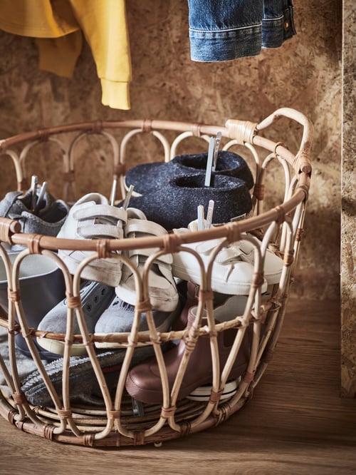 Hallway close-up of a round SNIDAD basket made of rattan storing multiple children shoes with grey KUNGSFORS magnetic clips.