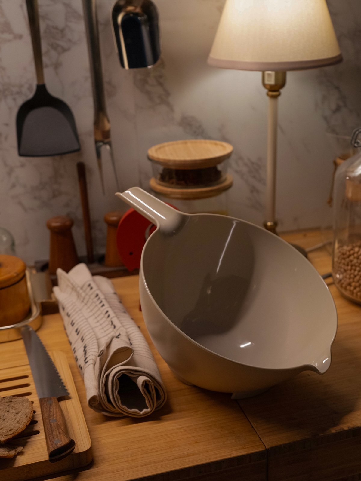 Una grande ciotola grigia posata su un piano di lavoro in legno, accanto a tovaglioli piegati, un coltello da pane e altri utensili da cucina.