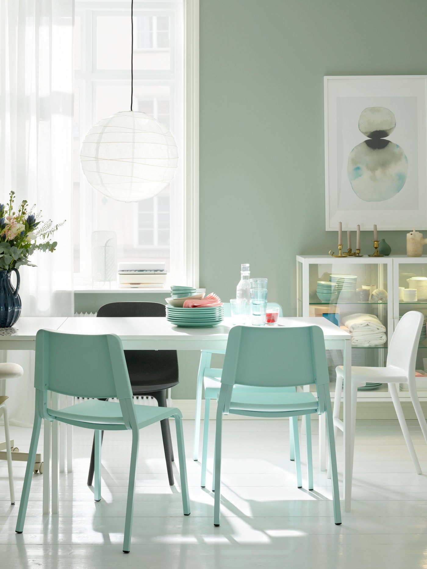 Una zona de comedor con una mesa MELLTORP blanca, una lámpara REGOLIT blanca y sillas de varios tipos.