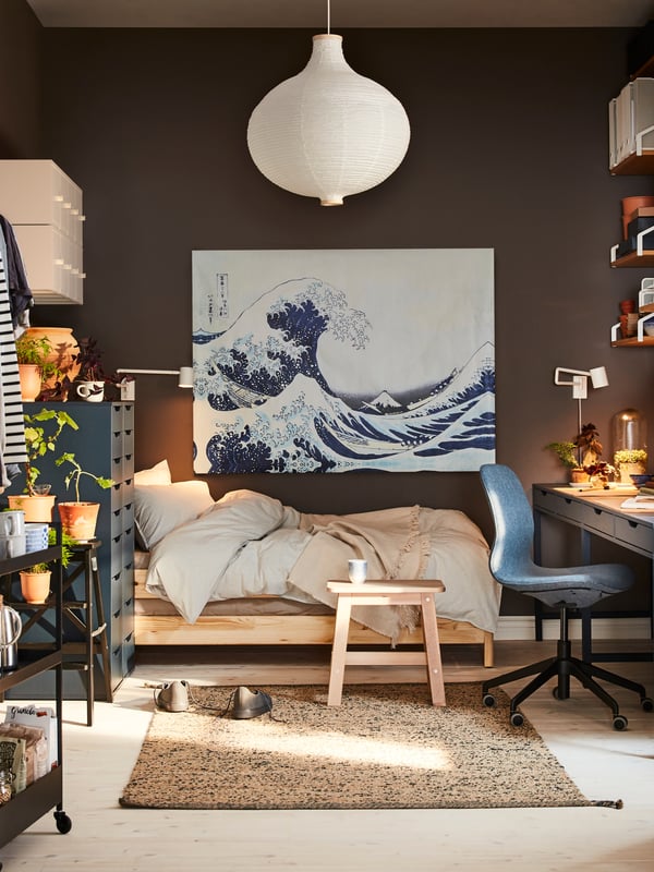 Una camera da letto con una scrivania e una sedia LÅNGFJÄLL illuminate da una luce NYMÅNE. Alla parete, c'è il quadro dell'onda giapponese. Dal soffitto, una lampda a sospensione RISBYN.
