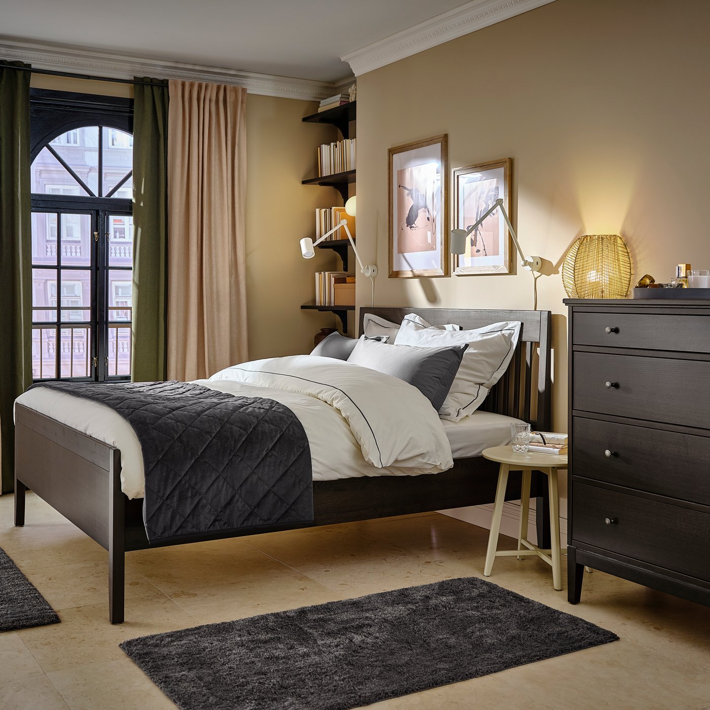 Una camera da letto sui toni del beige e del nero con un'ampia finestra con un bastone per tenda nero BEKRÄFTA. 