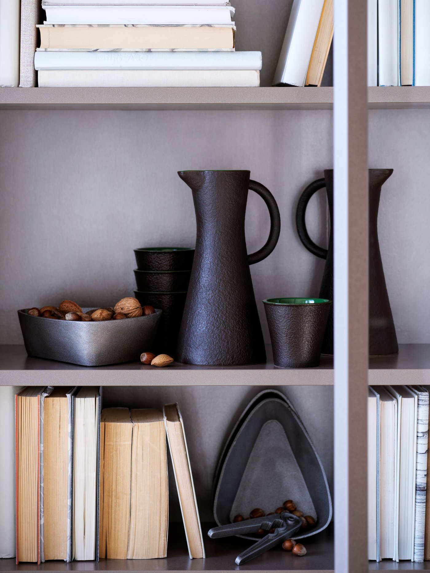 VINTER 2021 black stoneware jug is on a bookshelf with a bowl, mug and nutcrackers from the VINTER 2021 range.