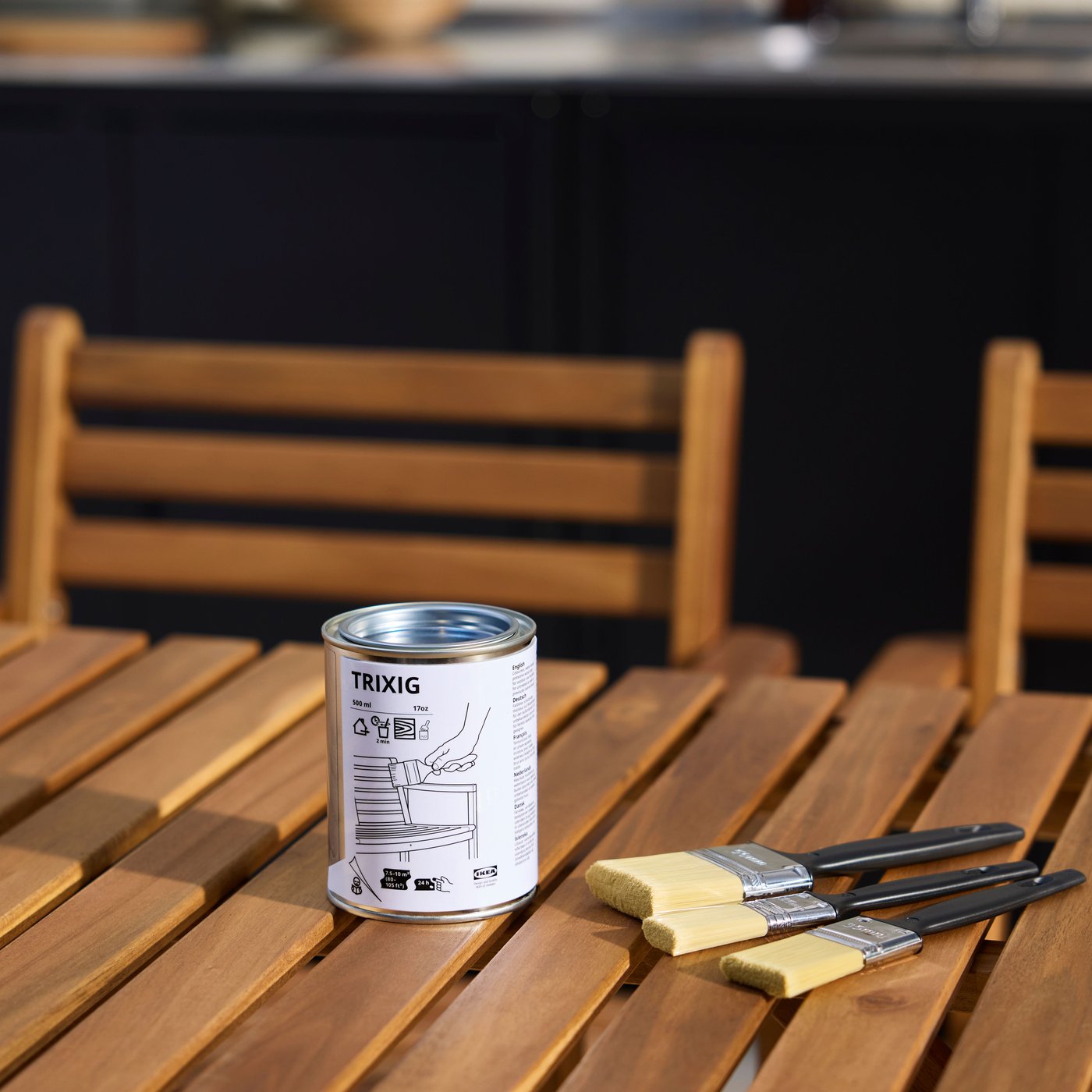 Puisen ulkopöydän päällä on kolme sivellintä TRIXIG-kuultomaalipurkin vieressä.