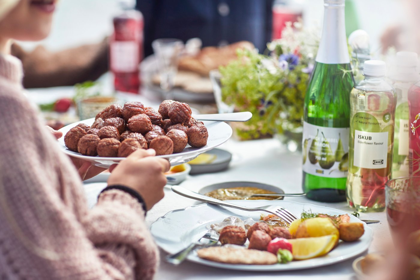 Una persona ha in mano un piatto con delle polpette svedesi ed è seduta ad una tavola apparecchiata