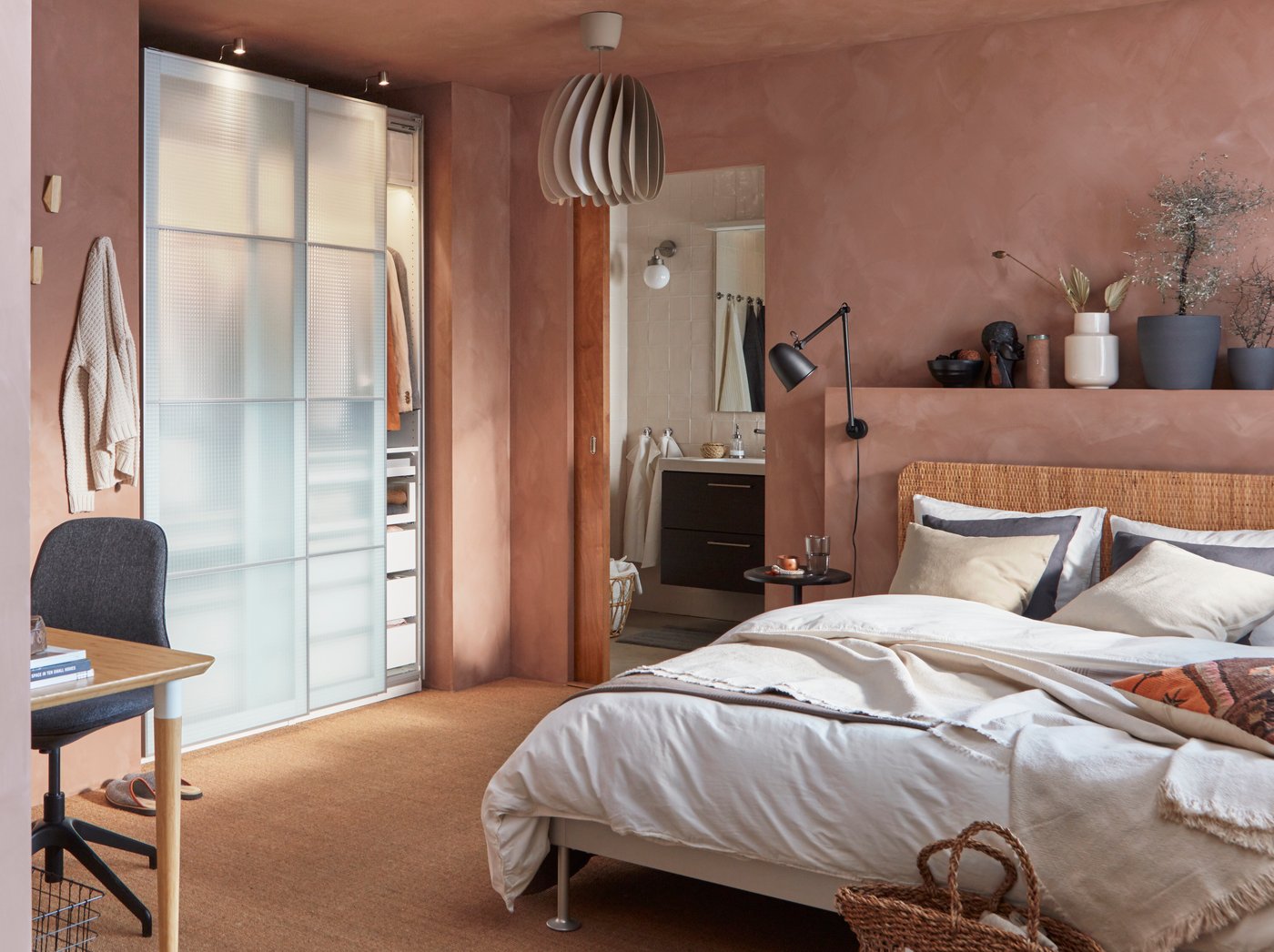 A PAX wardrobe with white translucent sliding doors in a bedroom furnished with pink walls and a queen-sized bed.