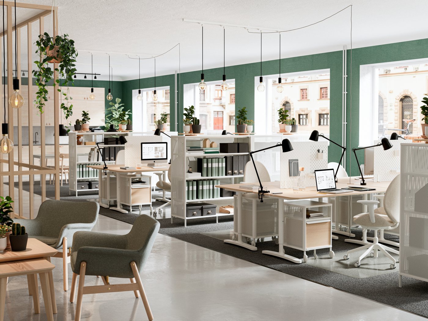 Ett öppet och ljust kontor med flera skrivbord, arbetsstolar och stora fönster som släpper in mycket dagsljus. Skrivborden är utrustade med skärmar och lampor, och rummet har gröna växter och en modern, luftig inredning.