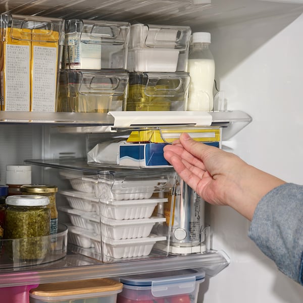 冷蔵庫の中で手が引き出し式の収納ケースを引き出している様子。周囲には牛乳パックや調味料、保存容器が整理されて並んでいる。