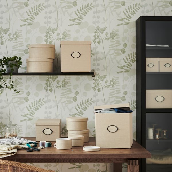 Beige KVARNVIK organizers in different sizes and shapes,  on a wooden table, a black shelf and in a black BILLY book case.