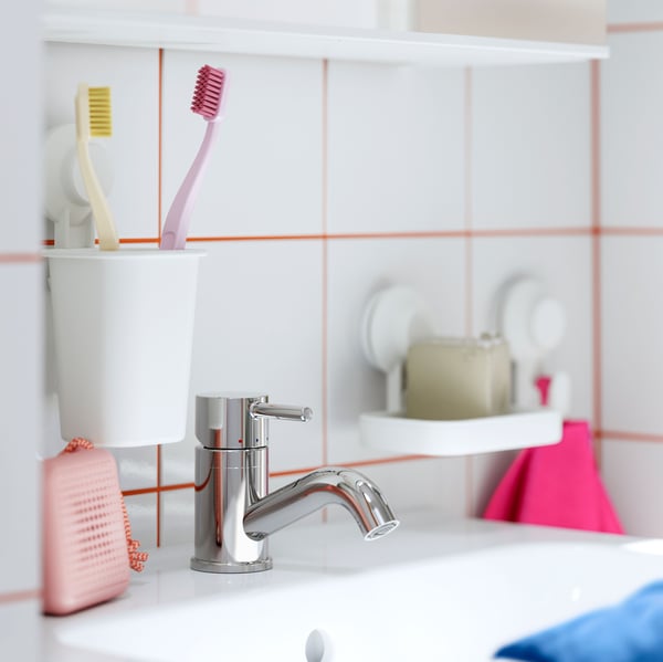 A bathroom with PILKÅN wash-basin mixer tap, toothbrushes in a holder, and soap dish on a white tiled wall with orange grout.