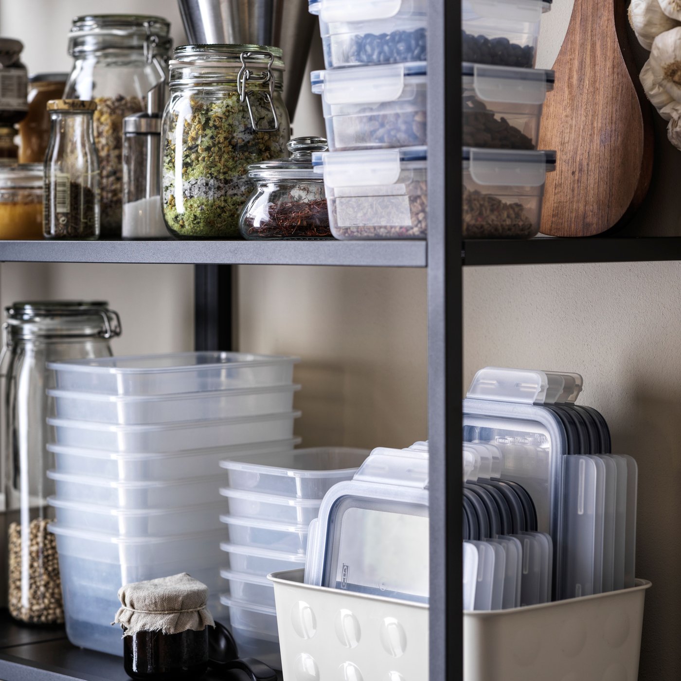 Hyllor med glasburkar och plastlådor fyllda med matvaror som spannmål och kryddor, samt större förvaringslådor.
