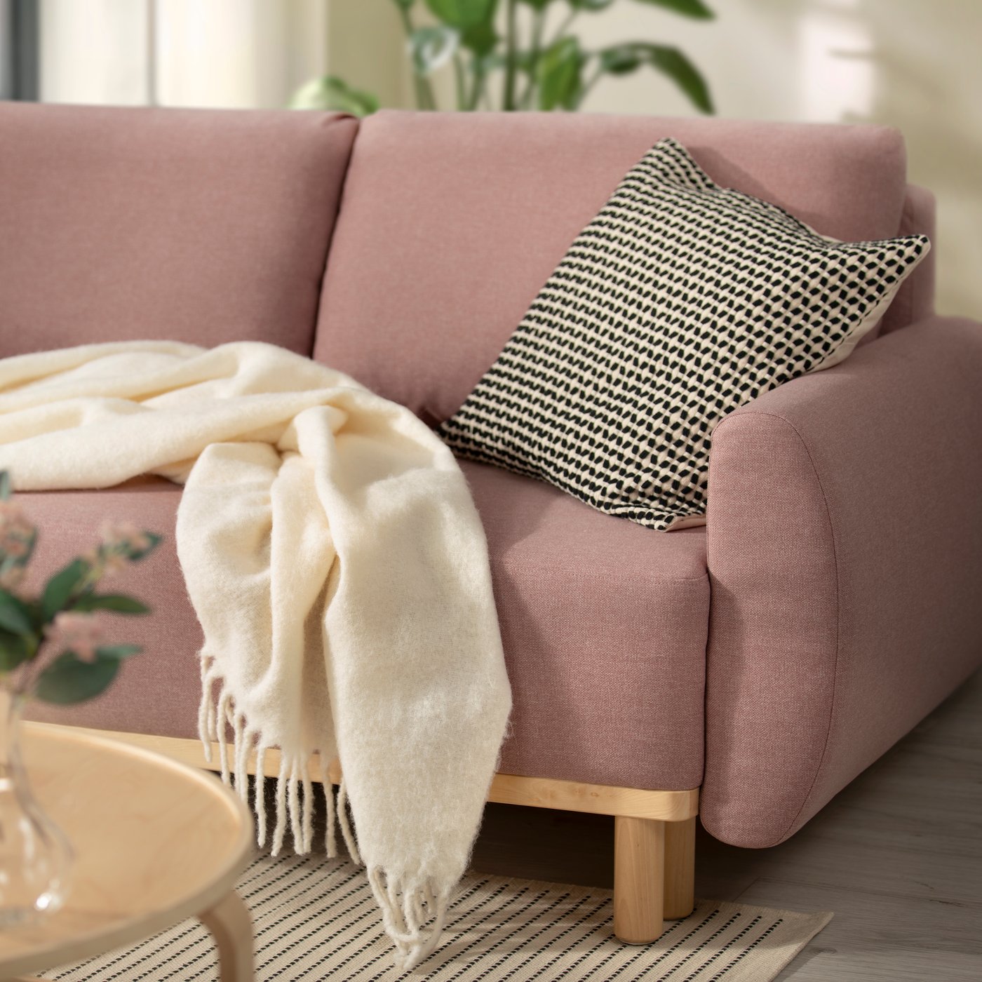 Poltrona in tessuto rosa con base in legno chiaro con un cuscino e una coperta