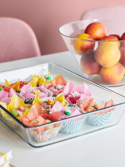 Sufragerie cu un vas dreptunghiular de servire a cuptorului din sticlă transparentă rezistentă la căldură, lângă un bol alb de servire a paharului.