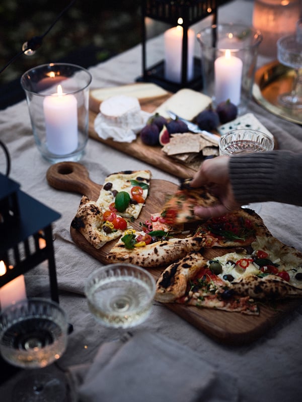 Bild tagen uppifrån på en person som tar en pizzaslice från en skärbräda i trä.