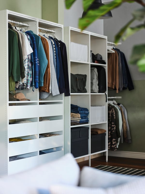 Two white AURDAL wardrobe combinations with hanging clothes and folded clothes and boxes on open shelves and in drawers.