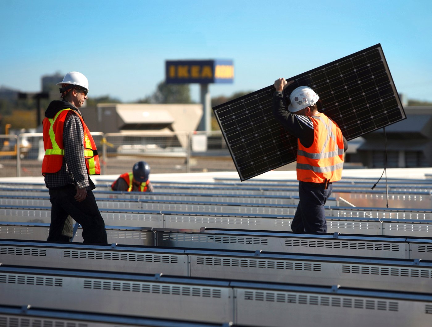People wearing safety wests are installing solar panels at an IKEA store.