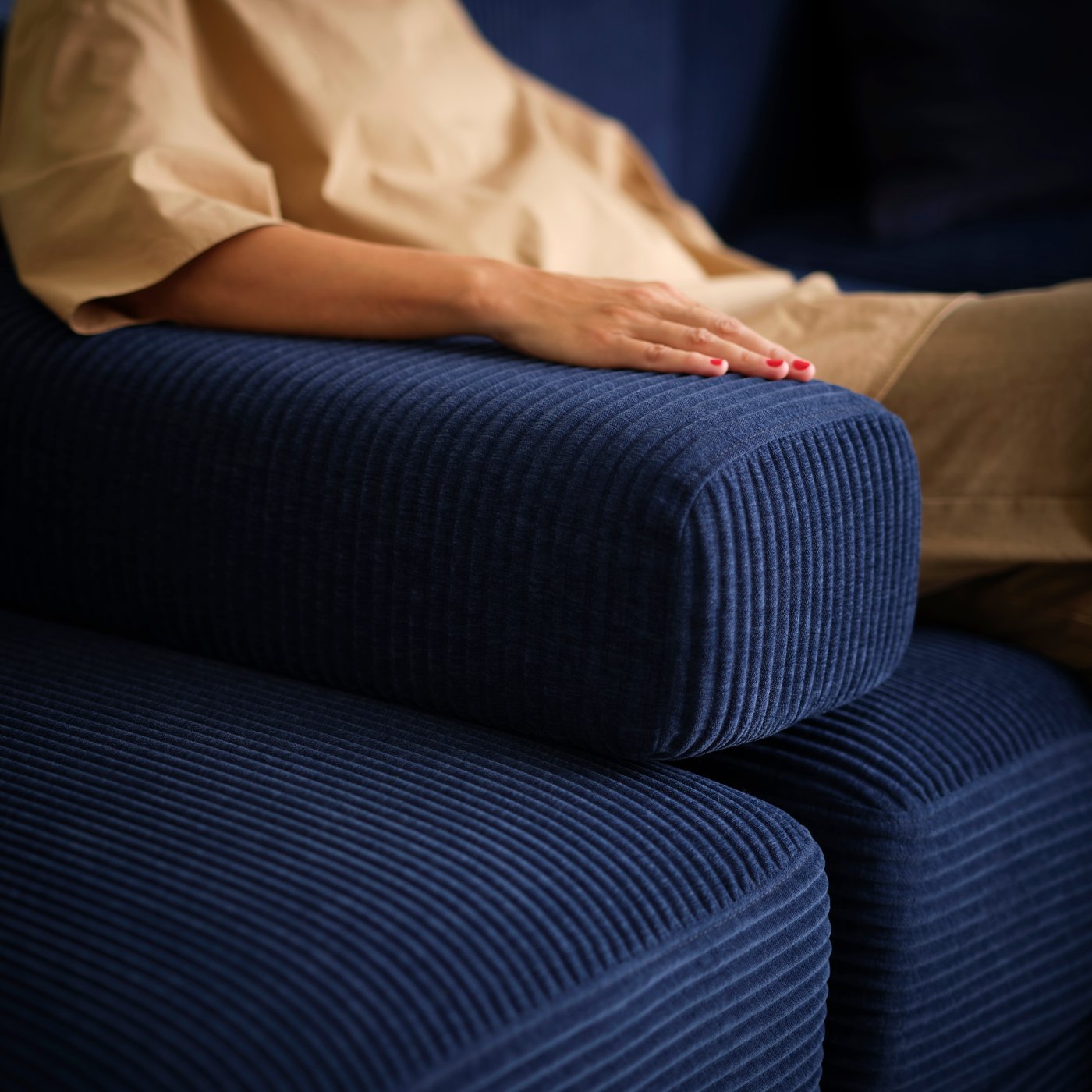 A person sits in a dark-blue JÄTTEBO four-seat modular sofa with their arm resting on a loose armrest placed in the sofa.