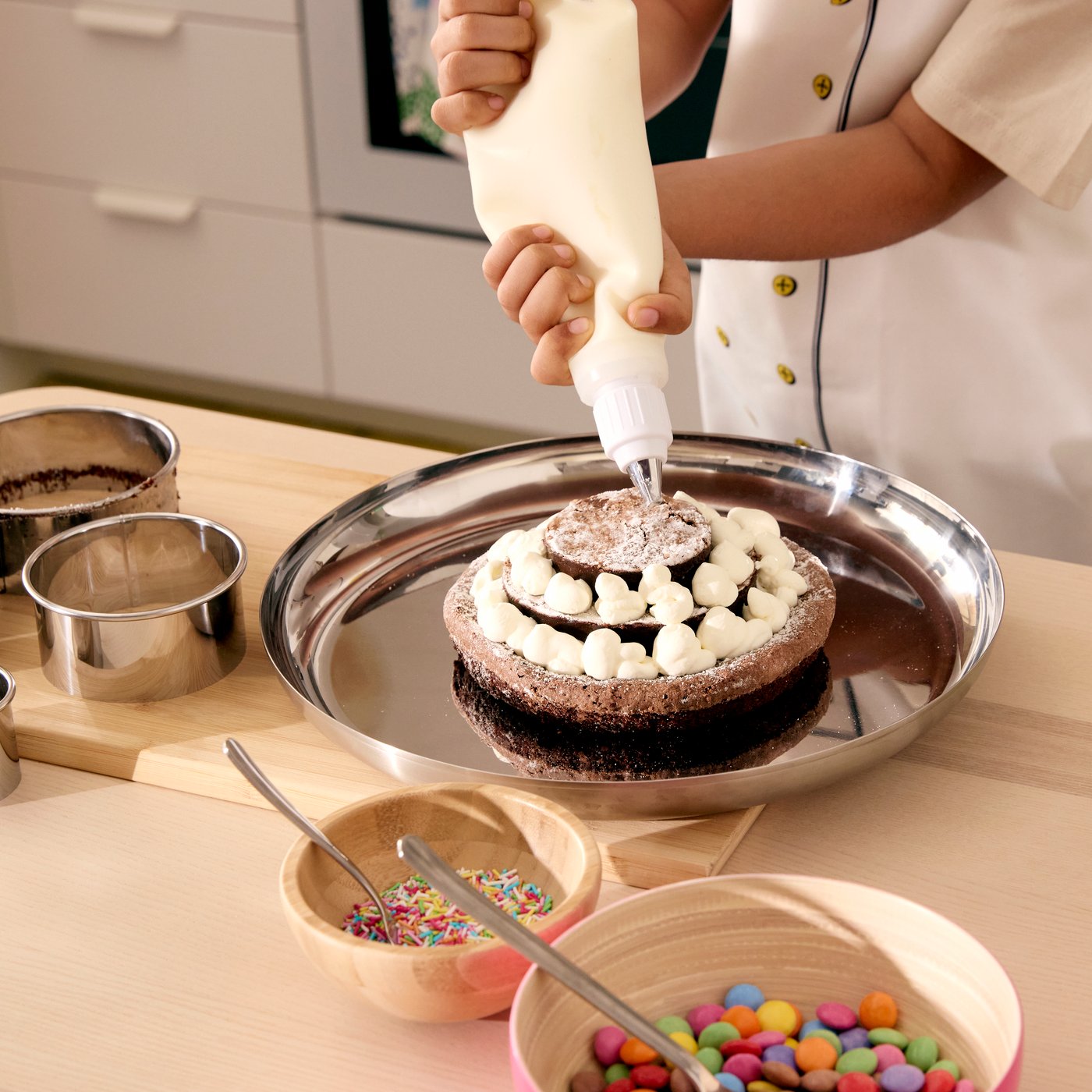 A chocolate cake in three layers, being decorated with little dots of cream with the help of SMAKSAM piping tool.