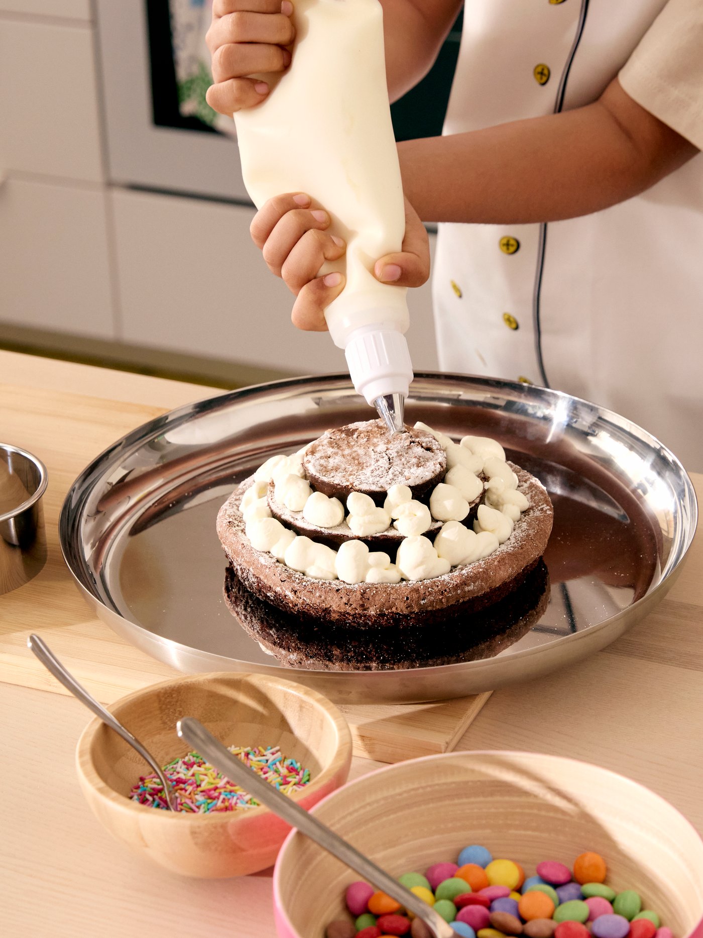 A chocolate cake in three layers, being decorated with little dots of cream with the help of SMAKSAM piping tool.