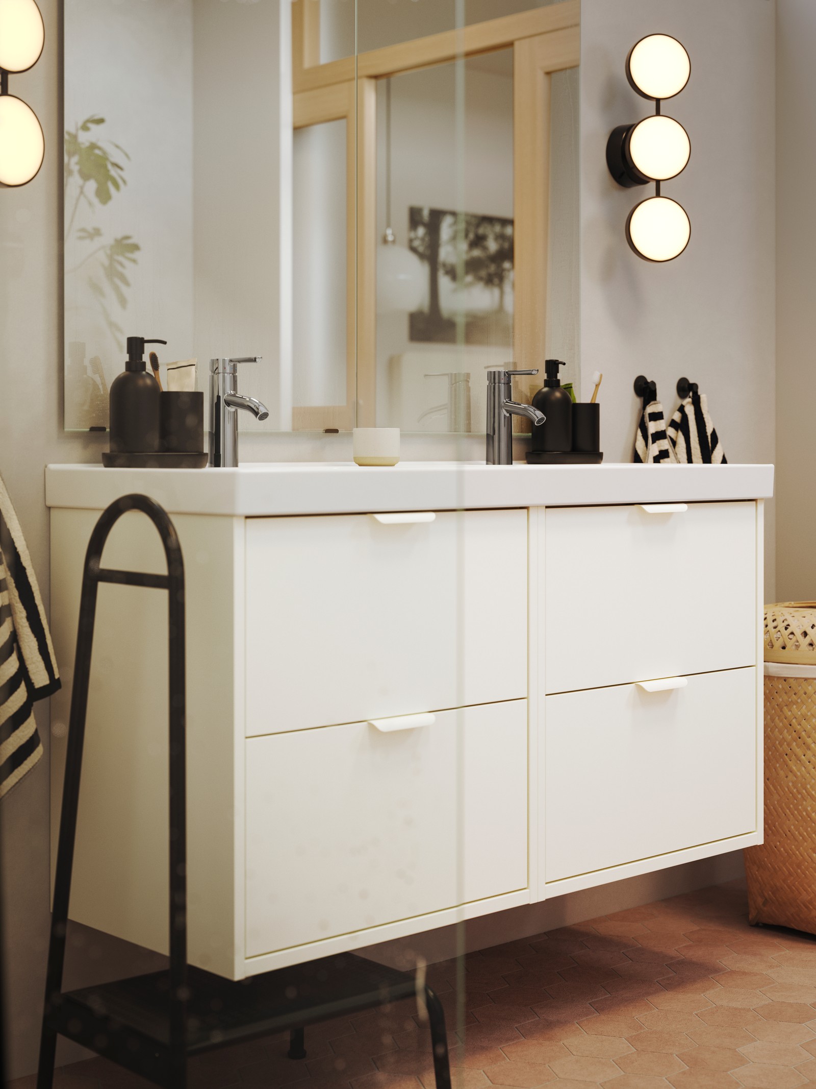 A bathroom has a two white HAVBÄCK wash-stands with drawers and a double ORRSJÖN wash-basin and a black KABOMBA wall lamp.