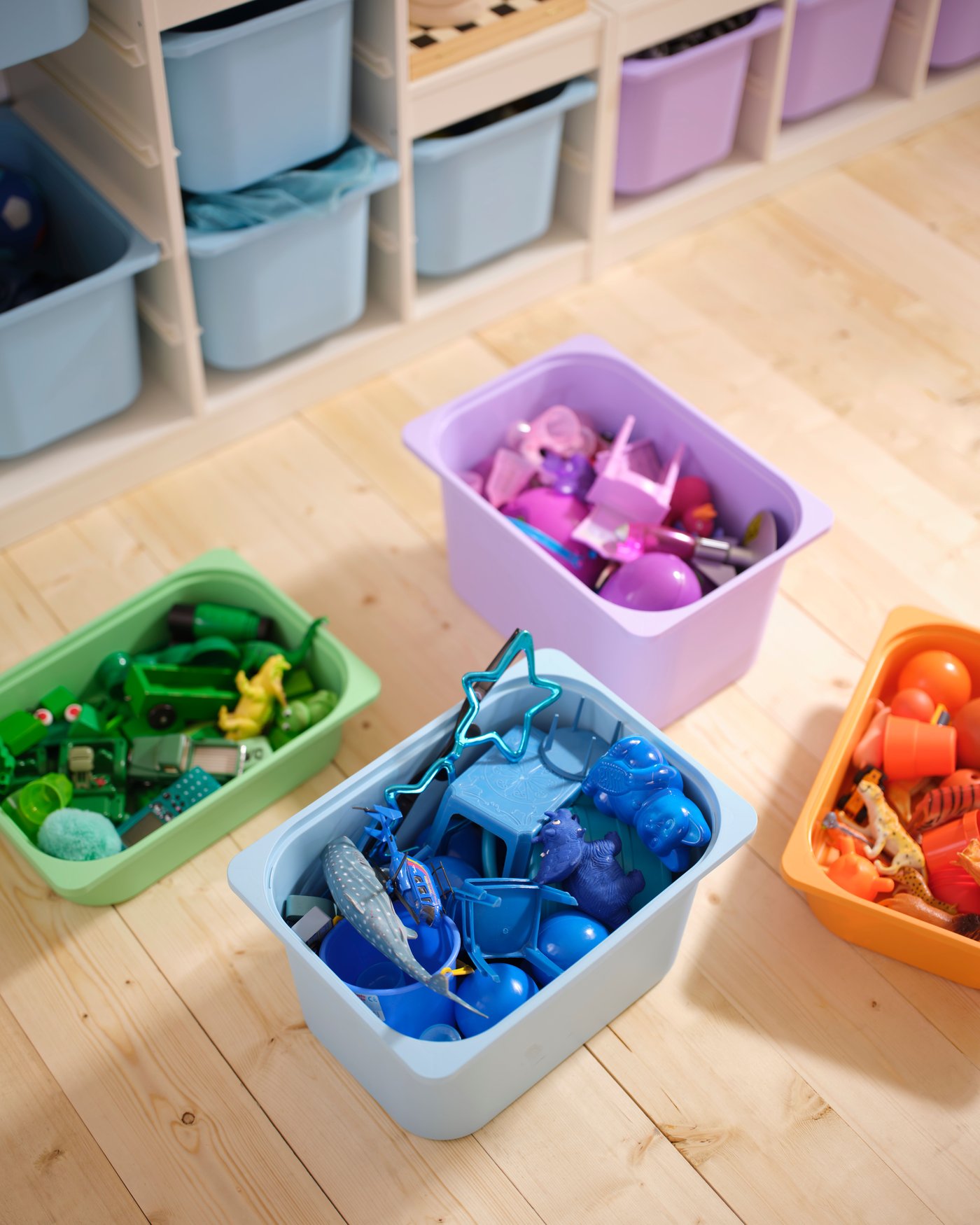 Four TROFAST boxes in light orange, light blue, light green and lilac are on the floor filled with toys, by a TROFAST frame.