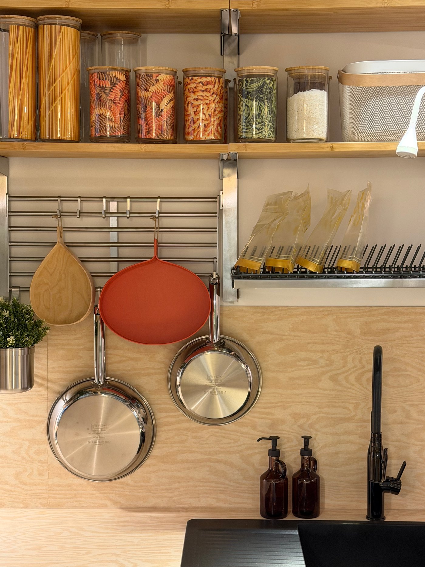 Des ustensiles de cuisine accroché au mur, un évier noir, des bocaux remplis