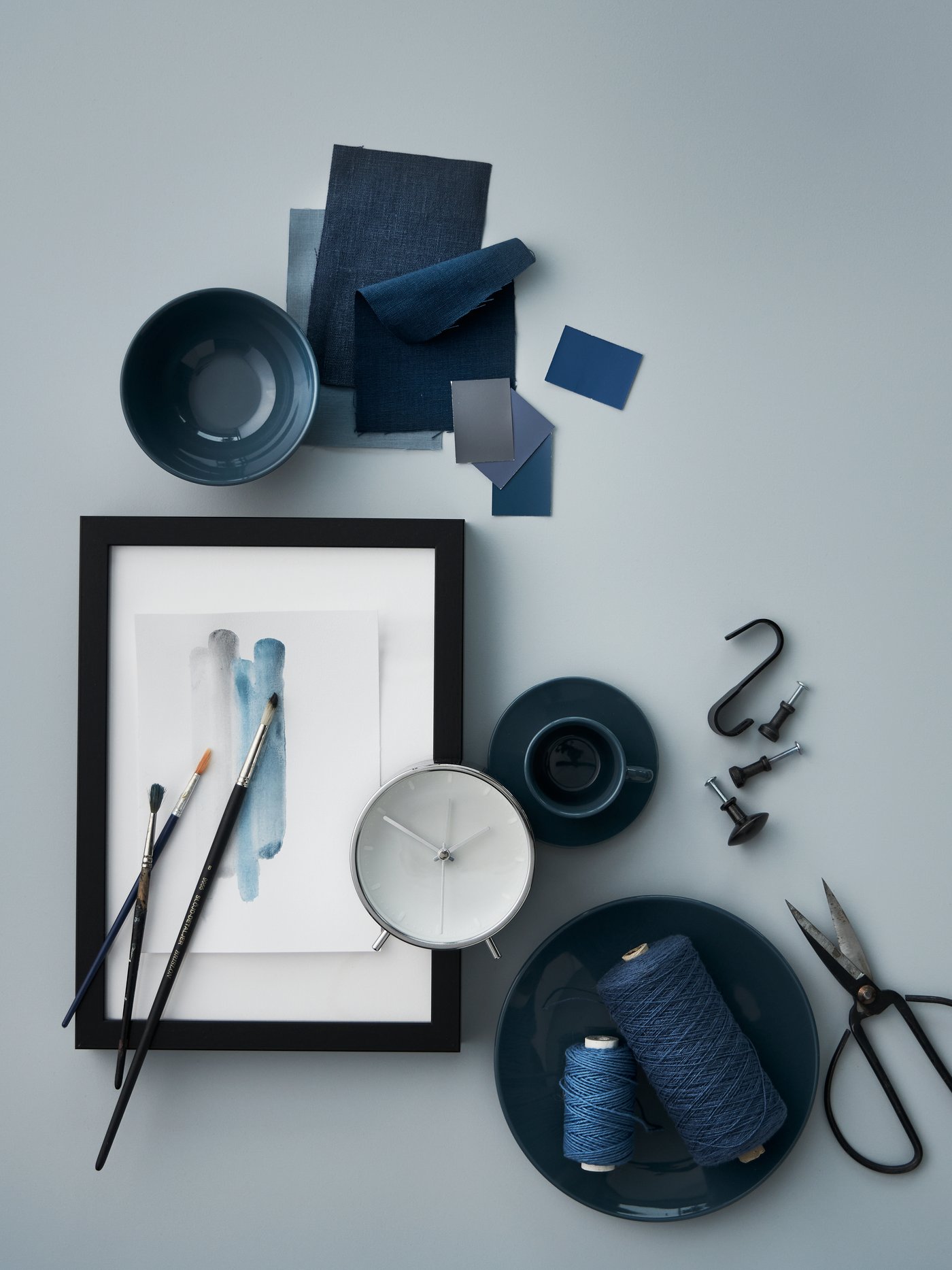 Una mezcla dispersa de objetos en tonos azules: una vajilla FÄRGKLAR de color turquesa oscuro, un despertador MALLHOPPA, cuerda y telas.
