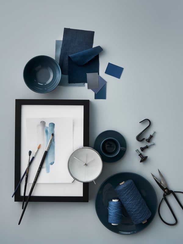 A scattered mix of items in shades of blue: dark-turquoise FÄRGKLAR tableware, a MALLHOPPA alarm clock, string and fabric.
