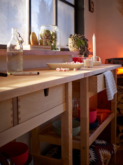Two birch FÖRHÖJA kitchen trolleys placed side-by-side on a wall like a long side table with a plate of sweets on it.