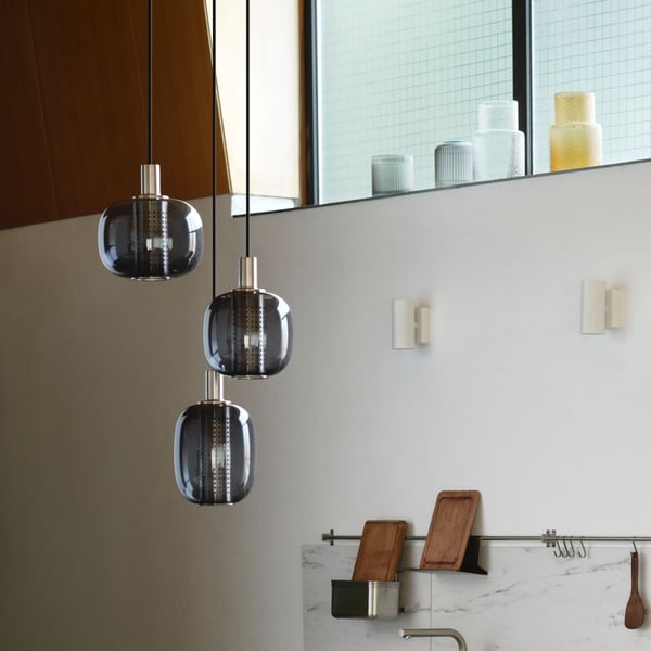 En HÖGVIND taklampa i nickelplätering/grått glas med 3 lampor hänger i ett utrymme i retrostil.
