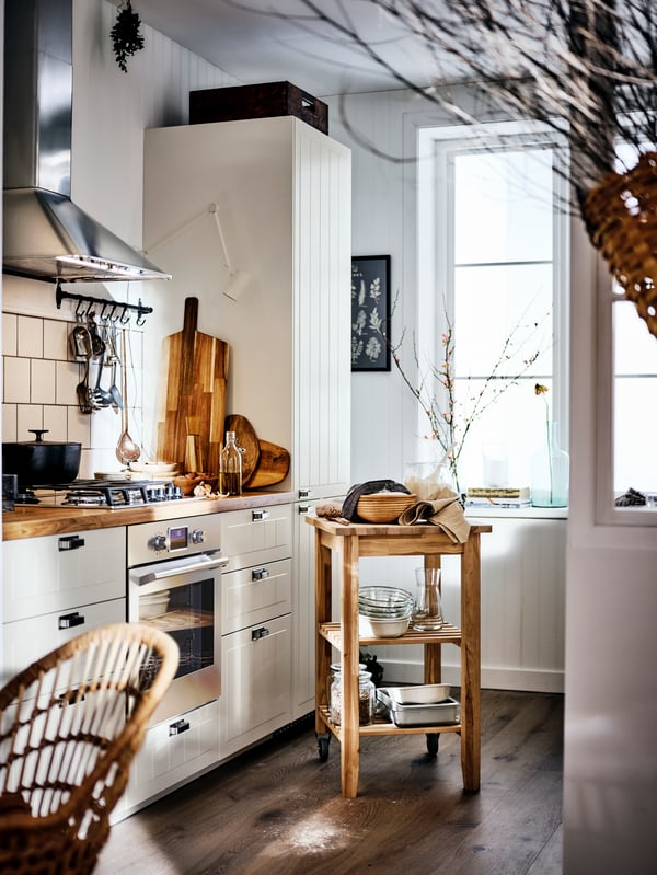 A country-style kitchen with a wood counter top and beige cabinets, and a birch trolley in the middle of the room.