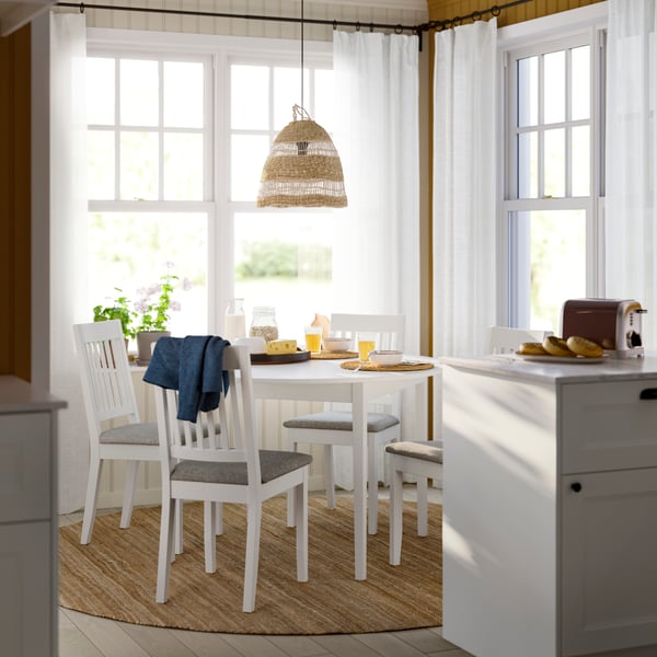 A bright dining area with a white dining table with four chairs, decorated with a blue throw, surrounded by natural light.