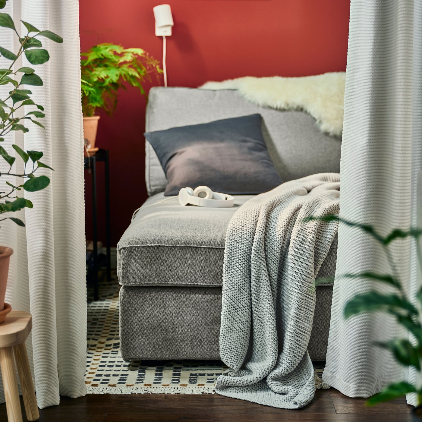 Šedá lenoška KIVIK se světle šedým plédem INGABRITTA, antracitovým polštářem a bílou nástěnnou lampou NYMÅNE.