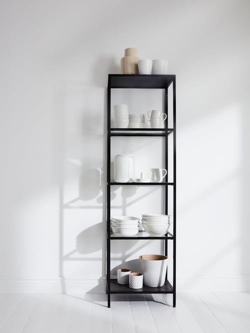 Une étagère VITTSJÖ brun noir/verre contenant des cache-pots, des bols et des tasses en porcelaine se trouve dans une pièce blanche.