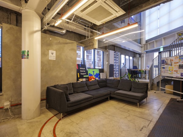 大きな窓に面したL字型ソファのラウンジ。壁にはポスターが貼られ、居心地の良い共用スペース