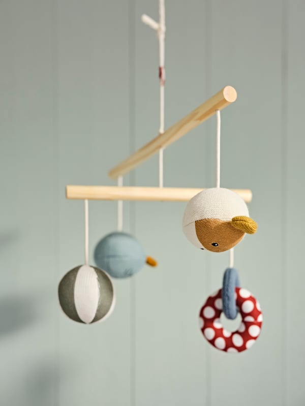 A GULDVAVÄRE mobile hangs in front of a green wooden wall. It has round animal characters and other shapes hanging from it.