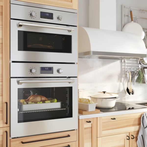 A SMAKSAK forced-air oven in black and roasting tin of food inside, and a SMAKSAK combi microwave oven in black above.