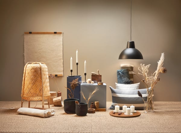 Un espace décoré avec ambiance présente un mélange d’objets décoratifs tels que des bougies, des coussins, des paniers et des fleurs séchées, éclairé par une suspension.
