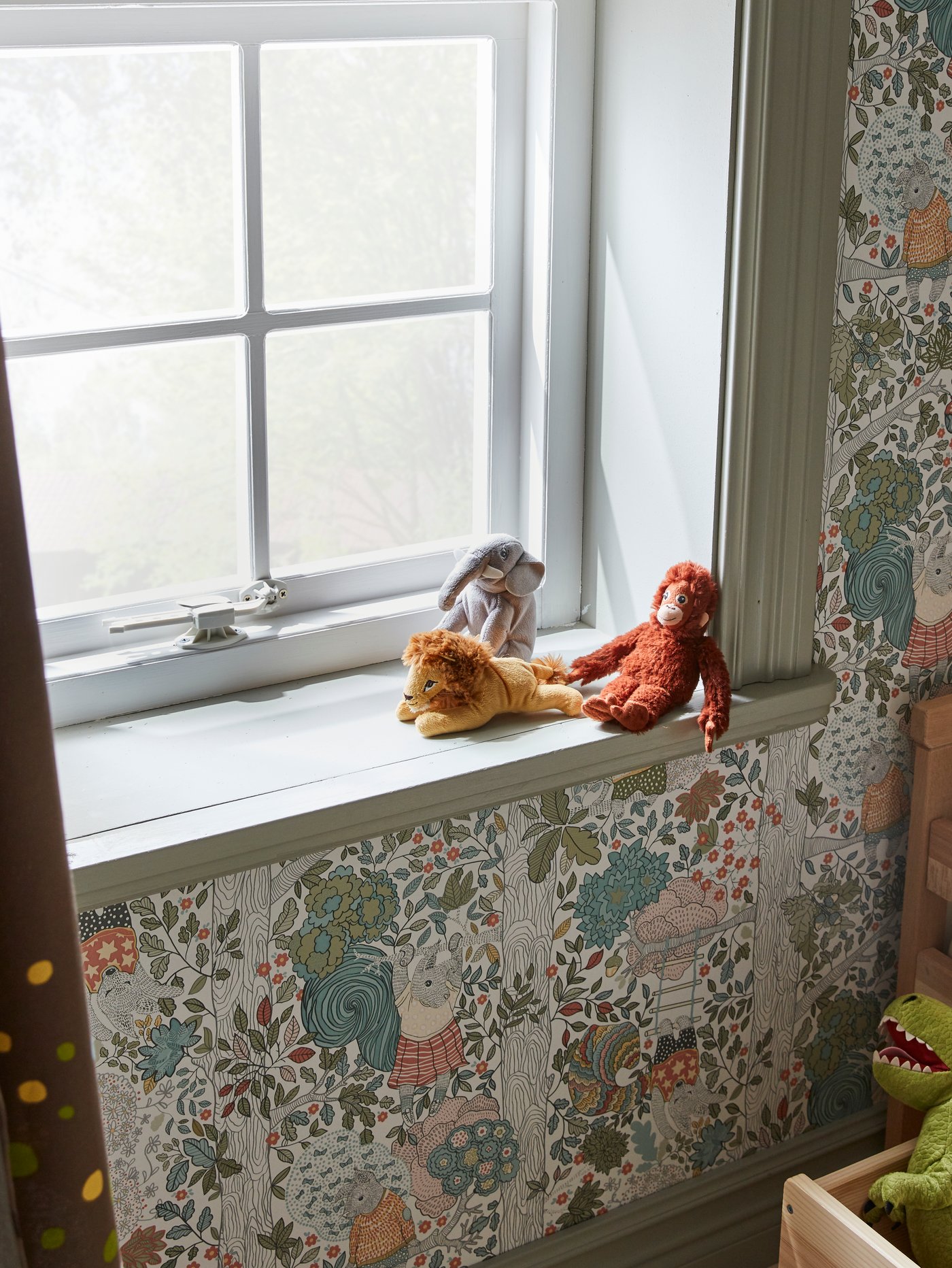 DJUNGELSKOG orangutan, lion and elephant soft toys sitting on a windowsill. The window is secured by a PATRULL window catch.