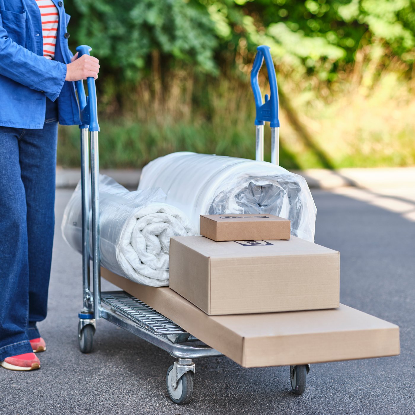 Several packages of furniture, a rolled-up mattress and a mattress topper are lying on an IKEA flatbed trolley.
