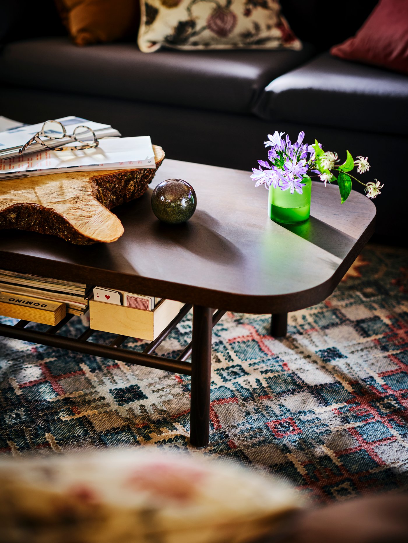 A small, green vase of purple flowers atop a LISTERBY coffee table with a brown stained oak veneer on a rug.