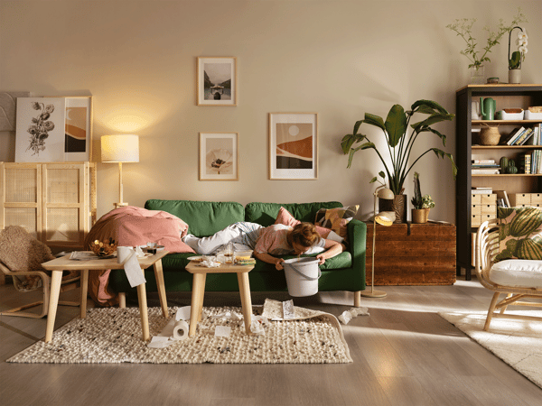 En stue hvor en kvinne ligger på en grønn sofa med en bøtte på gulvet.