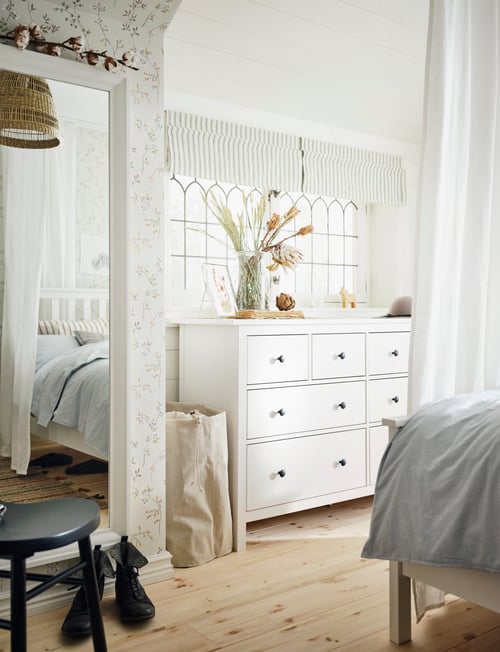 Bright bedroom with bed, large mirror, and white wooden chest of 8 drawers with classic traditional style and black knobs.