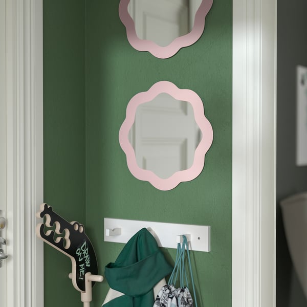 PRUNKHALLON pink wall mirror on a green wall, on top of a KUBBIS white rack with three hooks in the hallway
