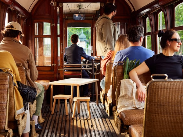 Two FLISAT stools and a FLISAT table on a tram surrounded by people.